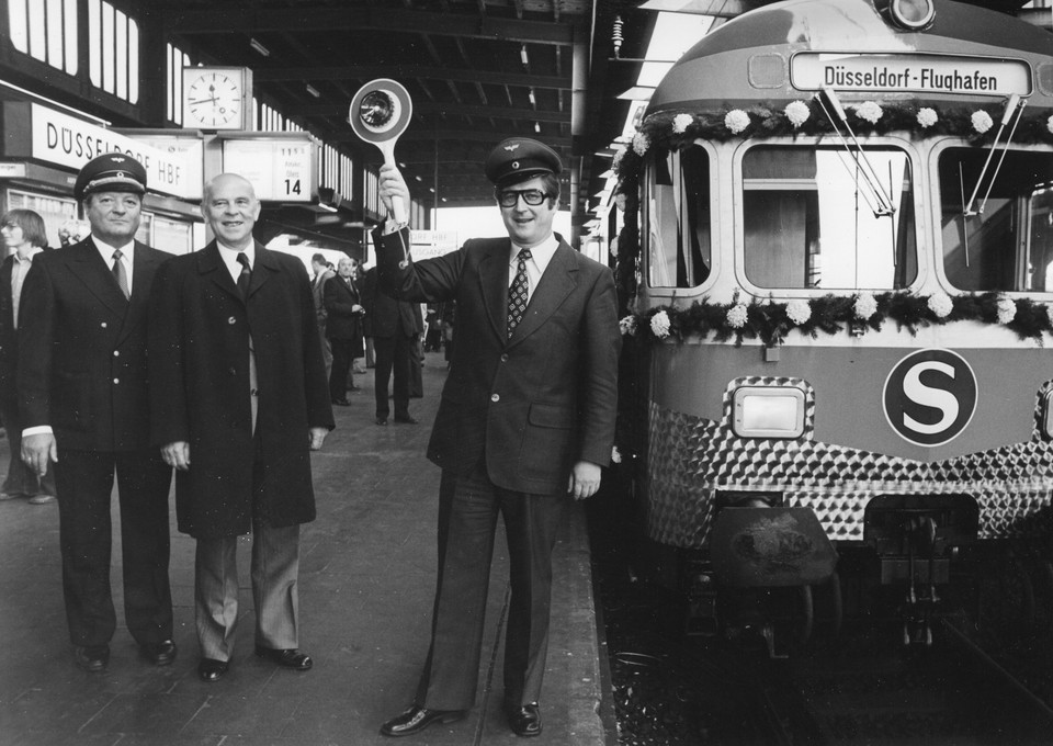 Historische Aufnahme einer S-Bahn am Düsseldorfer Hauptbahnhof. Vor dem Zug steht das Personal, der Kontrolleur hält eine Kelle in der Hand.